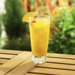Orange cocktail with maraschino cherry garnish, outdoor backyard setting.